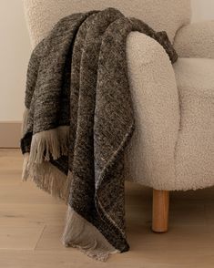 a chair with a blanket on top of it next to a white couch and wooden floor