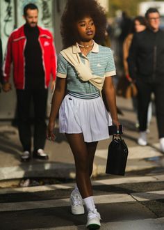 a woman walking down the street with an afro haircut and white tennis skirt on