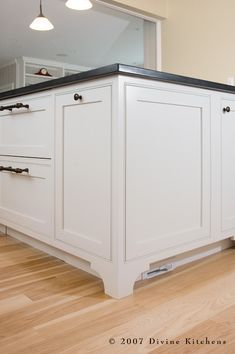 a kitchen with white cabinets and black counter tops in the middle of hardwood flooring