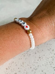 "MAMA BRACELET -This is for one MAMA bracelet. -This bracelet is a great, neutral frosted clear color that is shown in the pictures with gold beads beside the word and a red heart. -This bracelet is a stretchy material and is easy to get on and off. -This bracelet comes in small adult, medium adult or large adult sizes. The medium adult size is 7\" and is an average sized wrist. If you would like to measure your wrist size exactly, we can make it to your size! Just add how many inches your wrist Wedding White Heart Beads Bracelets, White Minimalist Personalized Name Bracelet, Adjustable White Name Bracelet With Heart Beads, White Hand-strung Name Bracelet With Round Beads, Hand-strung White Name Bracelet For Gift, Hand-strung White Name Bracelet As Gift, White Beads Bracelet, Bracelet Name, Mama Bracelet