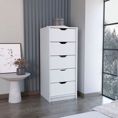 a white dresser sitting next to a bed in a room with a painting on the wall