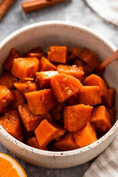 a white bowl filled with cubed sweet potatoes and an orange slice next to it