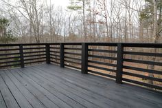 a wooden deck with black railings and trees in the background