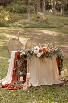 a table with candles and flowers on it in the middle of some grass next to two chairs