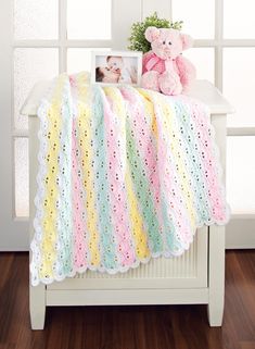 a crocheted baby blanket with a teddy bear sitting on it next to a window