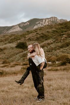 a man carrying a woman on his back in a field with mountains in the background