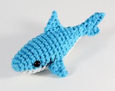 a crocheted blue and white shark toy on a white surface with black eyes