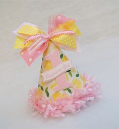 a pink and yellow birthday hat on top of a white surface with a ribbon around it