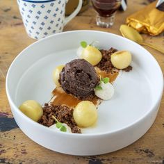 a white plate topped with ice cream and chocolate covered dessert on top of a wooden table