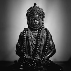 black and white photo of buddha statue with beads around his neck, sitting on the floor