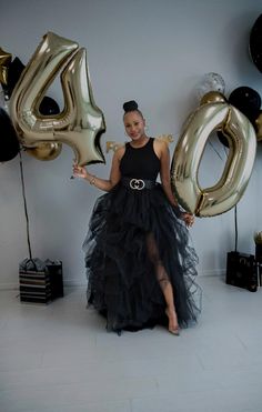 a woman in a black dress holding balloons and the number 50 is spelled with gold letters