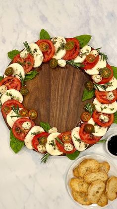 a wooden platter filled with sliced tomatoes and cheeses next to small bowls of dipping sauce