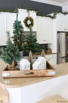 a kitchen with white cabinets and christmas decorations on the counter top, along with small trees