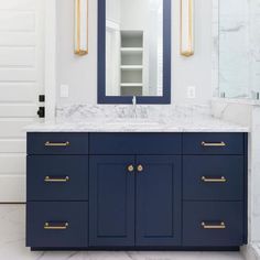 a bathroom vanity with marble counter top and blue cabinetry, along with gold pulls