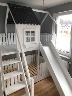 a white bunk bed with a slide next to it and a window in the background