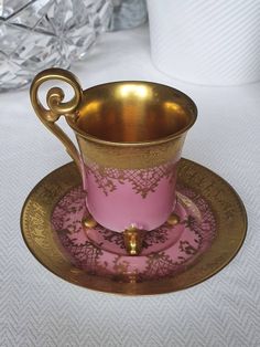 a pink cup and saucer sitting on top of a gold plate