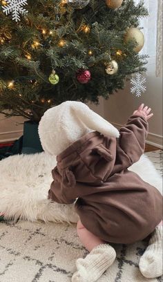 a small child in a brown outfit is playing near a christmas tree