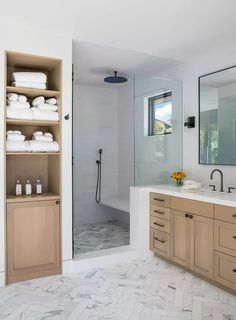 a bathroom with marble floors and wooden cabinetry in the shower area, along with white towels on shelves