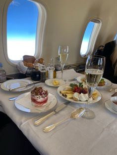 the table is set with food and wine for two people to enjoy on an airplane