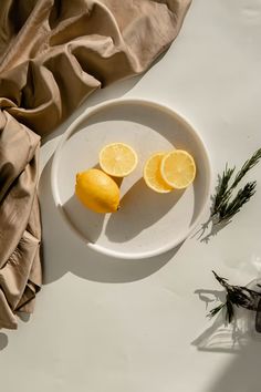 two lemons on a white plate next to some rosemary sprigs and a brown cloth