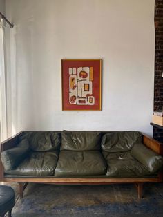 a green leather couch sitting in a living room next to a painting on the wall