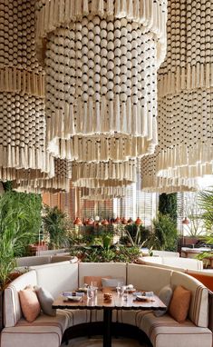 a restaurant with lots of hanging objects above the tables and booth seating, along with potted plants