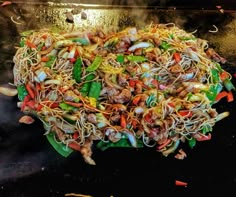 a large pile of noodles and vegetables on a grill with steam rising from the top