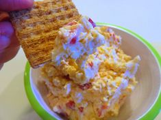 a person holding a cracker over a bowl of food