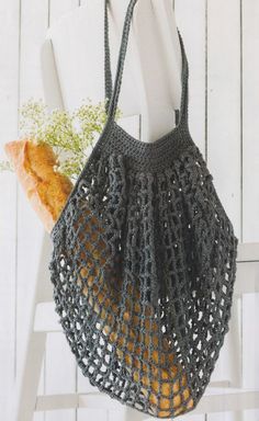 a crocheted bag hanging on a white chair next to a plant and an orange