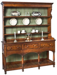 an old fashioned china cabinet with plates and cups on the top, sitting against a green wall