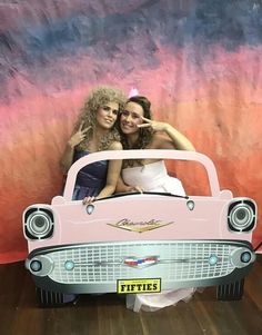 two women pose for a photo in front of a pink car with the word fifties written on it