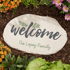 a welcome stone surrounded by flowers and plants