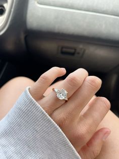 a woman's hand with a diamond ring on her finger next to a car steering wheel