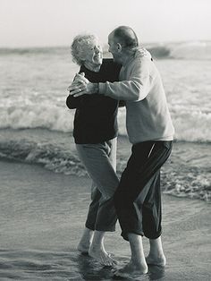 an older man and woman hugging on the beach