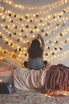 a woman sitting on top of a bed in front of a string of lights