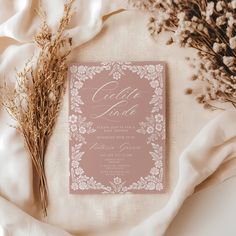 a pink and white wedding suite on top of a table next to dried flowers, with the bride's name printed on it