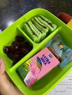 a person holding a green tray with food in it and two small containers filled with snacks