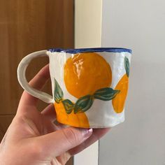 a hand holding a coffee cup with oranges painted on the outside and inside it