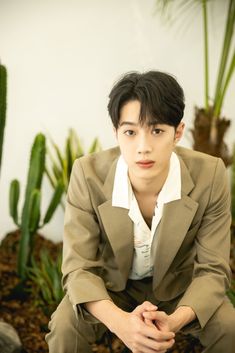 a young man in a suit sitting on the ground next to some cactuses and succulents