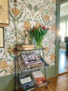 a table with books and flowers on it in front of a wallpapered room