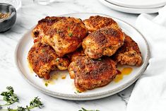 several pieces of chicken on a white plate with herbs and seasoning next to it