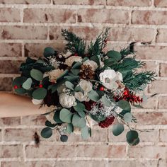 a woman holding a bouquet of flowers in front of a brick wall