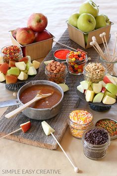 an assortment of fruits and snacks are arranged on a wooden tray with apples in bowls