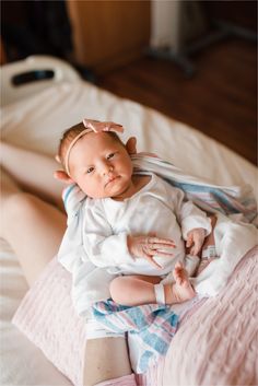 a woman holding a baby in her arms while laying on top of a white bed