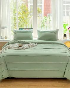 a bed with green sheets and pillows in front of a window