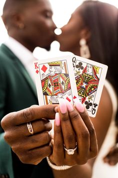 a bride and groom kissing while holding playing cards in front of their face with the other hand