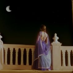 a woman in a purple sari is standing on a balcony looking at the moon