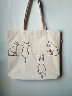 a tote bag with cats on it hanging from the side and one cat looking at another