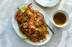 a white plate topped with shrimp and corn next to a bowl of dipping seasoning