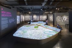 people are looking at an interactive map on display in a museum with black walls and flooring